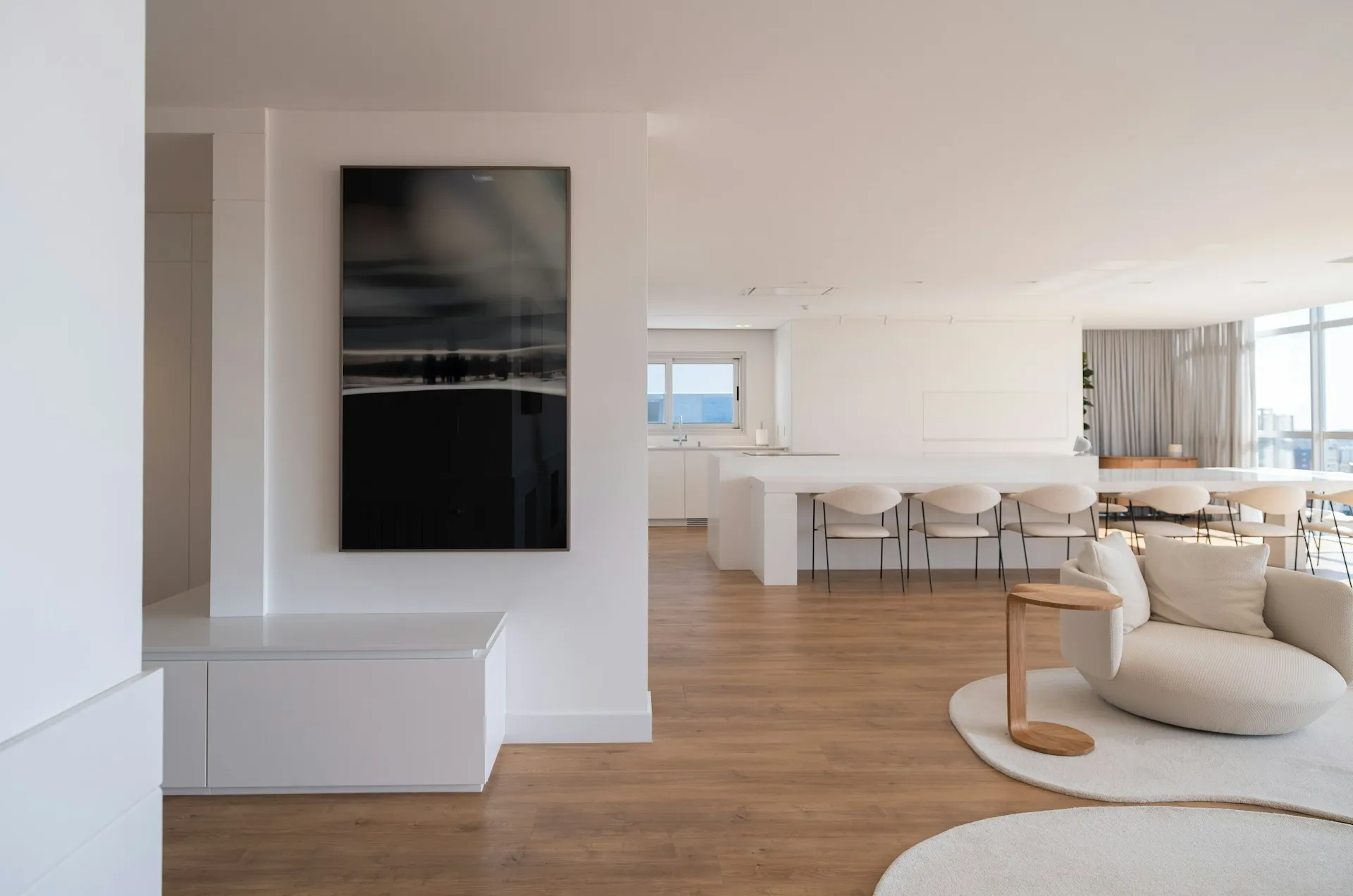 Bright, minimalist open-concept living and dining area with white furnishings, wood flooring, modern artwork, and floor-to-ceiling windows.